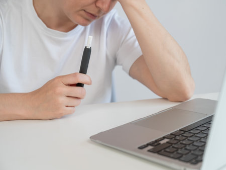 Tired woman smoking an electronic cigarette while working on a laptop. Tobacco heating systemの写真素材