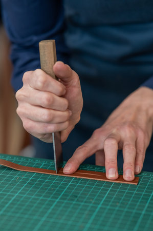 Woman tanner processes the edges of a leather belt in a workshop