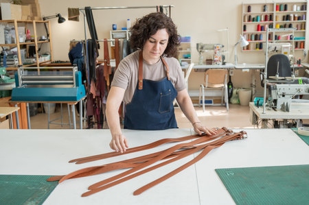 Caucasian woman makes belts from genuine leather in a workshop