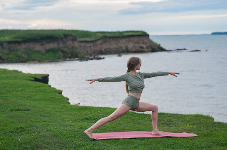 Caucasian woman doing yoga on the river bank. Warrior poseの写真素材