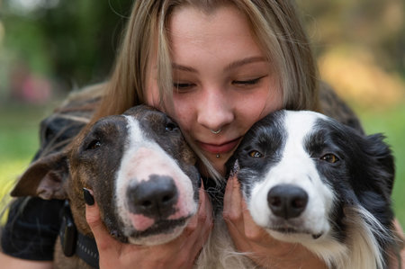 This heartwarming image captures a person joyfully holding two affectionate dogs close to their...