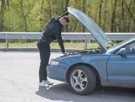 Caucasian man looking under the hood of his car