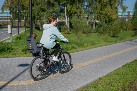 Caucasian woman riding bicycle with toddler son sitting behind her in child seat in park
