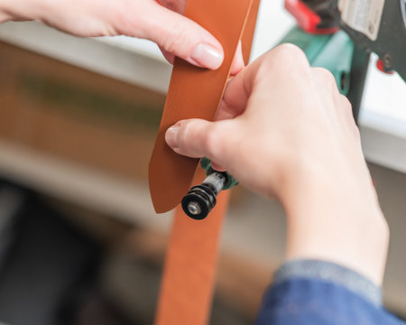 Leatherworker grinding the edge of a strip of leather for a belt in the workshop