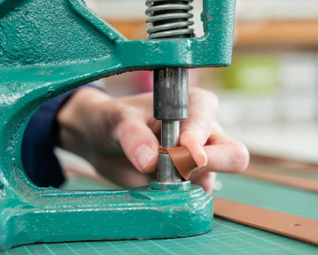 A woman attaches accessories to a leather belt. Leatherworkers workshop