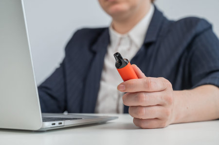 Faceless businesswoman smokes disposable vape and works on laptop