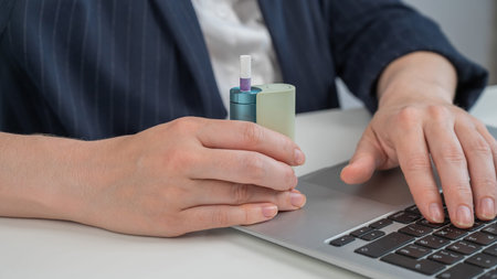 Business woman using an electronic cigarette while working on a laptop.