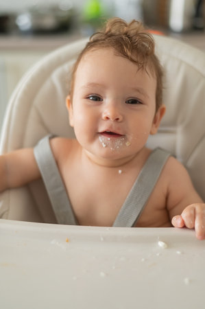Cute baby boy smeared in sour cream sits in a high chairの写真素材