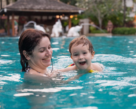 Caucasian woman holds son while swimming in pool on vacationの写真素材