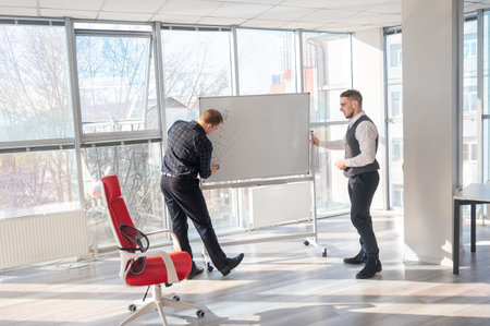 Two Caucasian men discussing work at a white board