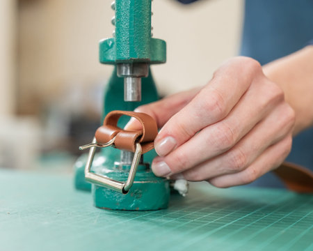 A woman attaches accessories to a leather belt. Leatherworkers workshop