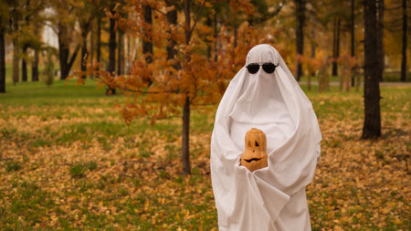 Woman in white sheet holding jack olantern against autumn forest background. Halloween costumeの写真素材