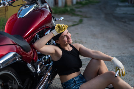Brunette woman in denim shorts repairs a red motorcycleの写真素材