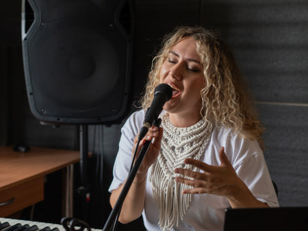 Caucasian woman singing into microphone and playing synthesizer and recording herself on laptopの写真素材