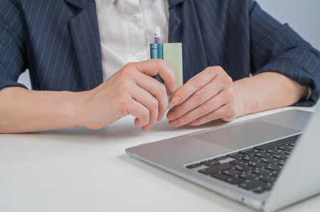 Business woman using an electronic cigarette while working on a laptop.の写真素材