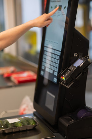 A woman weighs cucumbers at a self-service checkoutの写真素材