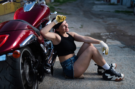 Brunette woman in denim shorts repairs a red motorcycleの写真素材