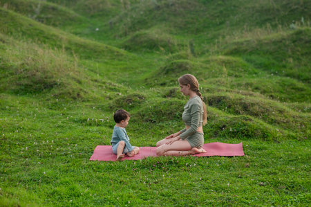 Caucasian woman doing yoga with her little son outdoorsの写真素材