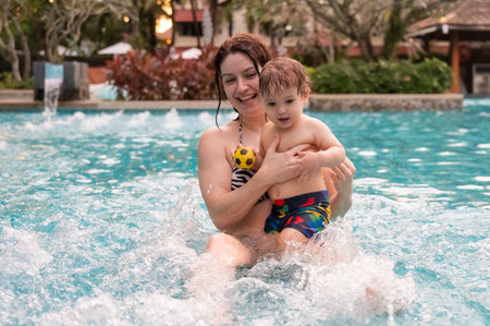 Caucasian woman holds her son while swimming in a pool on vacation. Mom teaches little boy to swimの写真素材