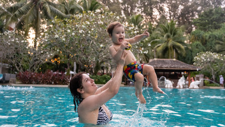Caucasian woman holds her son while swimming in a pool on vacation. Mom teaches little boy to swim