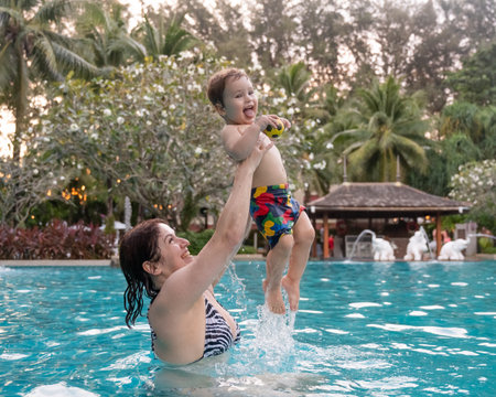 Caucasian woman holds her son while swimming in a pool on vacation. Mom teaches little boy to swimの写真素材