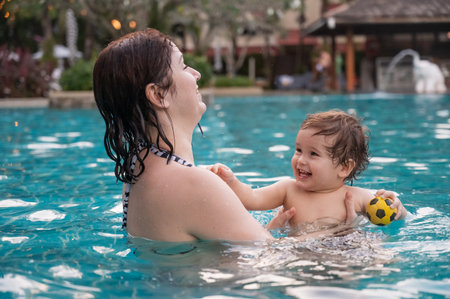 Caucasian woman holds her son while swimming in a pool on vacation. Mom teaches little boy to swimの写真素材