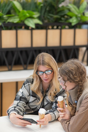 A mother and her teenage daughter eat ice cream at a shopping mall food court