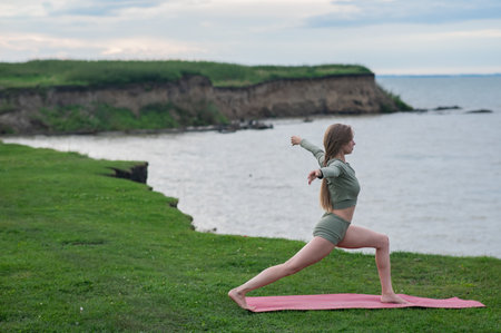 Caucasian woman doing yoga on the river bank. Warrior poseの写真素材