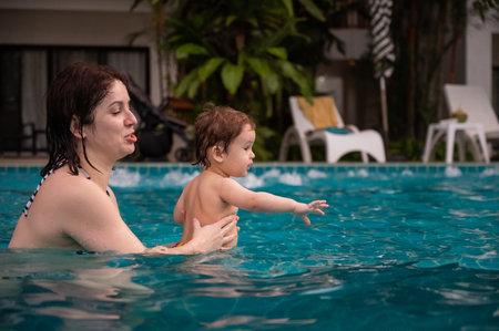 Caucasian woman holds her son while swimming in a pool on vacation. Mom teaches little boy to swimの写真素材