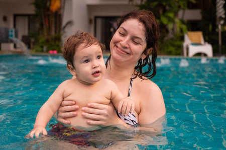Caucasian woman holds her son while swimming in a pool on vacation. Mom teaches little boy to swim