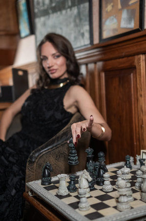 A beautiful brunette in a black evening dress plays chess