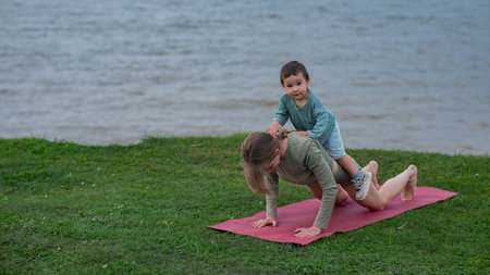 Caucasian woman doing yoga with her young son on the river bankの写真素材