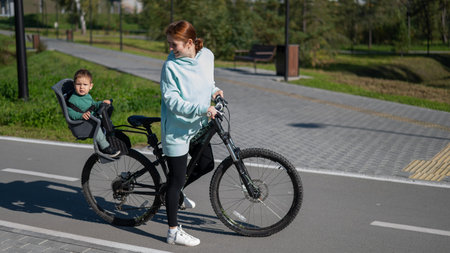 Caucasian woman rides bicycle with one-year-old son in park
