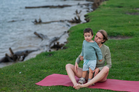 Caucasian woman doing yoga with her young son on the river bankの写真素材