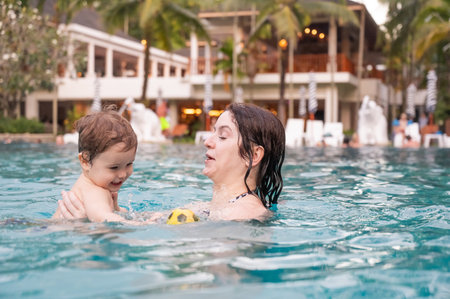 Caucasian woman holds son while swimming in pool on vacationの写真素材
