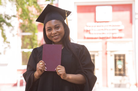 Happy young african woman in graduation gown holding diplomaの写真素材