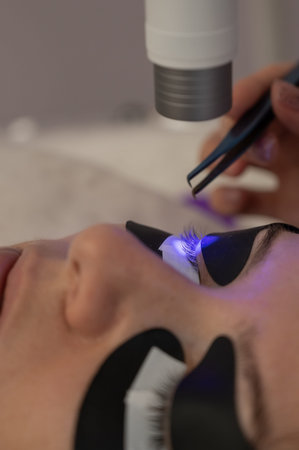 A woman undergoing eyelash extension procedure using an ultraviolet lamp
