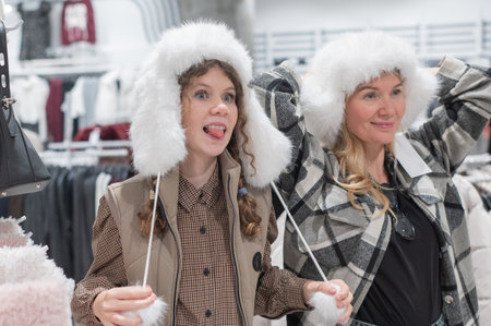 A mother and her teenage daughter shop for winter hats at a shopping mallの写真素材