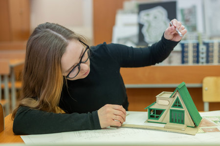 Caucasian young woman making a model of a building. Student of the construction university