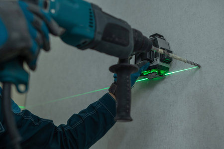 A man measures distances with a laser level and drills into a wall with a hammer drill