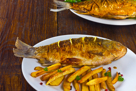 fried fish with fries on a white plate on a wooden tableの写真素材