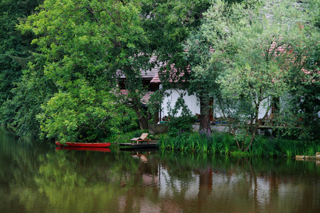 a quiet place on the water with a red boat, cottage and trees in backgroundの写真素材