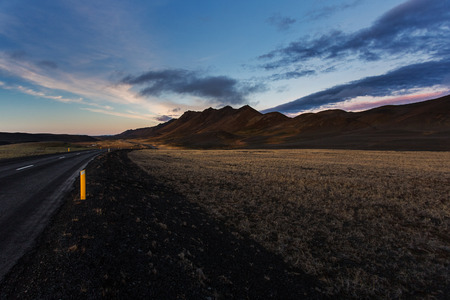 Dark road in north Iceland at sunset. Mountains on the horizon, dark blue sky, bollards on roadの写真素材