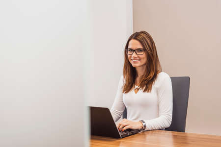 Businesswoman working on laptop, front view. Smile. Happy business woman sitting at deskの写真素材