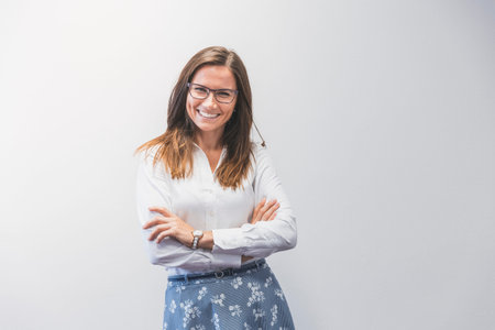 Businesswoman in the office. Young woman with glasses standing with folded arms, front view, white...
