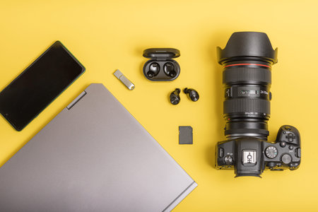 Workspace with camera, laptop, mobile phone, headphones on yellow background. Flat lay photographer...