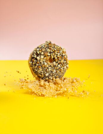 Chocolate doughnut with nuts topping captured mid air falling with nuts flying from groundの写真素材