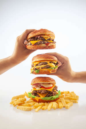 Two hands holding a gourmet cheese burger on top of one another with beef burger with potato chips on the bottomの写真素材