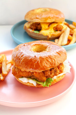 Crispy breaded fried chicken brioche donut bun burger served with hand cut fries on pink plate.の写真素材