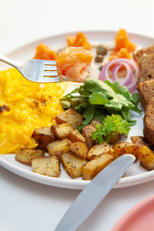 Smoked salmon with dill cream capers and scrambled eggs with rye bread and veggies.の写真素材